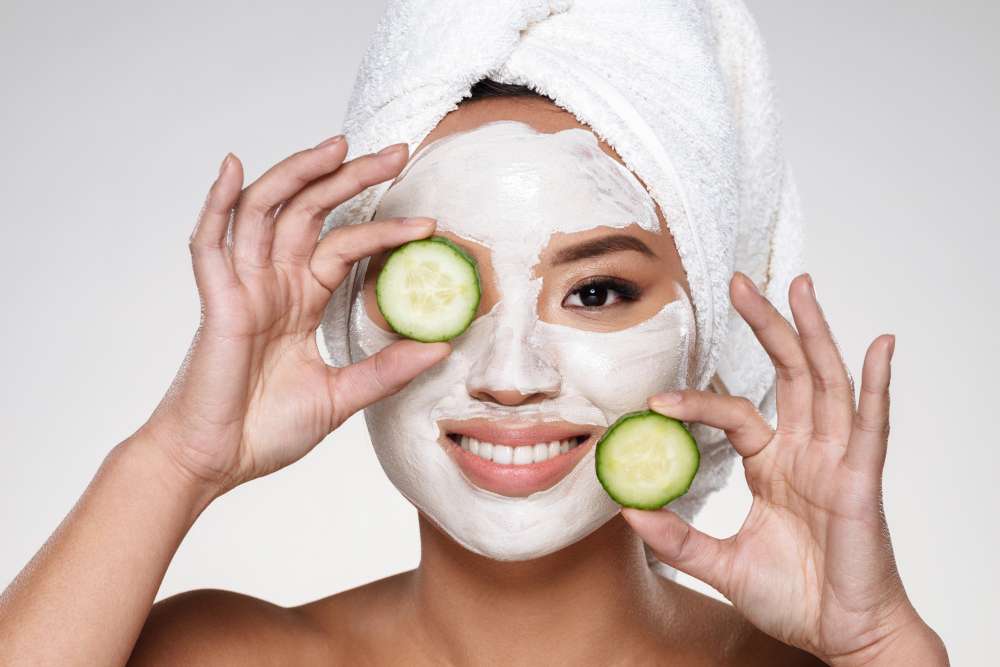 Lady with deep cleanser on face holding cucumber slices.